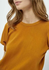 Senapsgul stickad topp med en figurnära silhuett, rund halsringning och korta ärmar. Mjuk textur och subtilt ribbat detaljer vid kanterna.