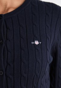 Cardigan blu navy lavorato a trecce con bottoni e piccolo logo a scudo ricamato sul petto.