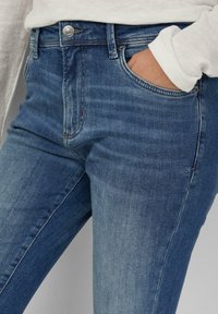 Blaue Denim-Jeans mit einem subtilen Farbverlauf, ausgestattet mit einem klassischen Fünf-Taschen-Design, Metallknopfverschluss und leichtem Ausbleichen an der Vorderseite.