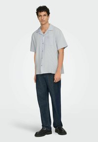 Kortærmet skjorte med krave i lys blå ternet mønster, med en brystlomme og blå knapper, parret med mørk denim bukser.