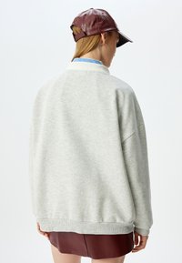 Sudadera de color gris claro con un corte holgado, puños acanalados y dobladillo. Combinada con una gorra brillante de color burdeos. Textura suave, diseño casual.