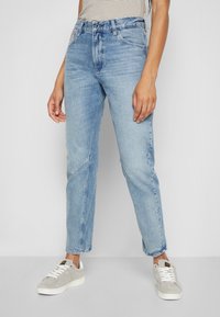 Ljusblå denimjeans med hög midja, rak ben och urtvättade detaljer. Kombinerat med grå mockasneakers och en randig topp.