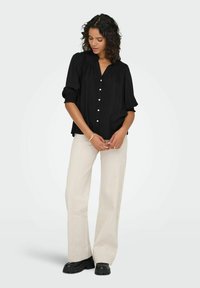 Sort skjorte med korte, puffede ærmer og plisseret design, parret med løse, cremefarvede bukser og sorte chunky sko.