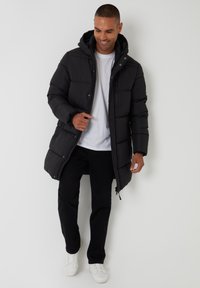 Black padded coat with a hood, featuring a zip front and snap buttons. Paired with black pants and white sneakers. Smooth texture.