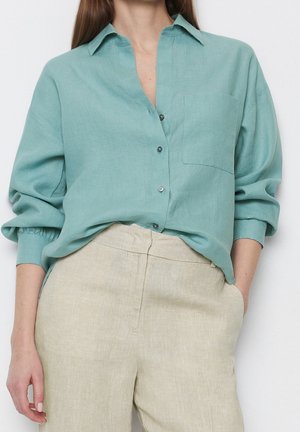 Light teal linen shirt with a collar, front pocket, and button closure, paired with beige linen trousers for a relaxed fit.