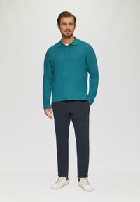 Türkise Langarm-Polohemd mit Kragen, kombiniert mit dunklen Hosen und weißen Sneakers. Glatte Textur, minimalistisches Design, keine sichtbaren Muster.