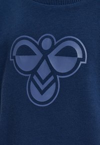 Granatowy materiał z teksturą posiada duże, stylizowane logo pszczoły w jaśniejszym odcieniu niebieskiego, umieszczone centralnie dla kontrastu, z graficznymi liniami podkreślającymi wzór.