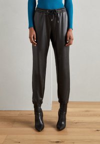 Zwarte leren joggers met een elastische tailleband en enkels, gecombineerd met puntige zwarte hoge hakken en een geribde blauwe lange mouw top.