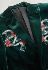 Emerald green velvet jacket with a black interior, featuring detailed embroidery of a snake and flowers in red and blue on the front.