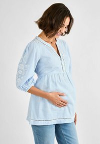 Blusa premaman a righe azzurro chiaro con dettagli floreali bianchi ricamati sulle maniche, scollo a V e vita arricciata.