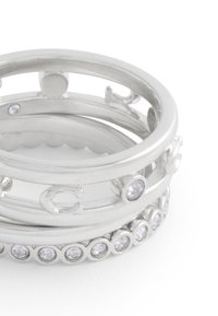 Conjunto de tres anillos de plata que presentan piedras preciosas transparentes. Dos anillos son lisos con diseños en forma de corte, y uno tiene una fila de pequeñas piedras redondas.