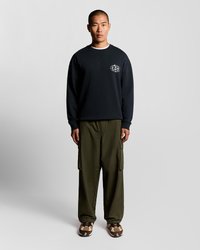 Sweatshirt preta com logótipo no peito, calças cargo oliva com bolsos laterais e ténis estampados. Design simples e descontraído.