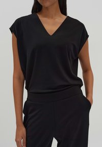 Zwarte V-hals top met korte mouwen, gemaakt van een gladde stof. Eenvoudig ontwerp met een losse pasvorm, gecombineerd met bijpassende zwarte broek.