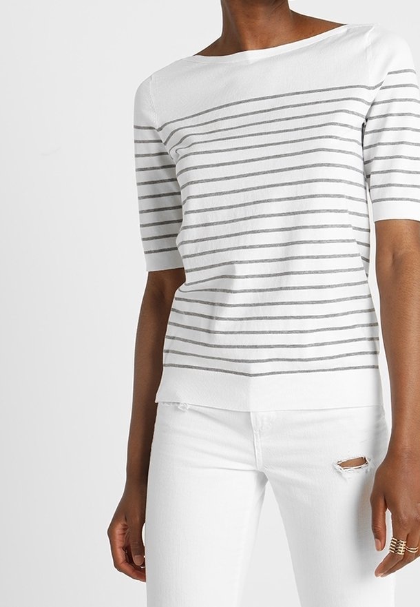 Bílý top s krátkými rukávy se šedými vodorovnými pruhy, výstřihem na loď a volným střihem. Kombinován s bílými džíny s distressed efektem.