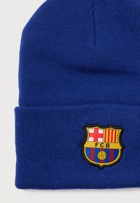 Gorro de punto azul con vuelta; escudo del club Barcelona bordado en detalles amarillos, rojos y azules. Textura suave, tejido ligero.