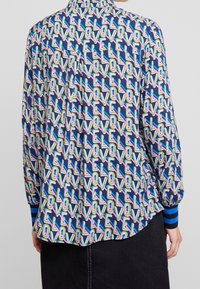 Nappikauluksellinen paita, jossa sininen pohja ja värikäs "LOVE"-kuvio. Pitkät hihat raidoitetuilla kalvosimilla. Kevyt kangas.