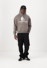 Gray hooded sweatshirt with white logo, paired with black cargo pants. Black cap and black sneakers with white stripes complete the outfit.