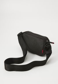 Schwarze Nylon-Umhängetasche mit glatter Textur, rechteckiger Form, Reißverschluss und verstellbarem Schultergurt. Mit rotem Logo-Highlight.