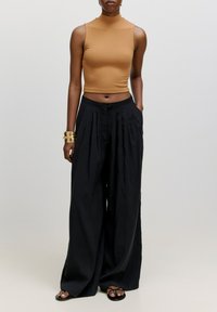 Hellblau gerippter Cropped-Top, kombiniert mit schwarzen weit geschnittenen Hosen mit vorderen Falten. Metallisches Armbandakzent am Handgelenk.