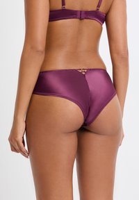 Ensemble de lingerie en satin violet à la texture lisse, avec un détail à bretelles croisées et un design sans couture à l'arrière.