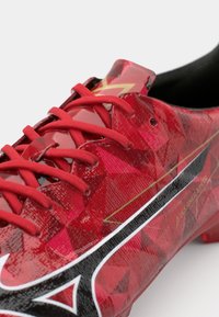 Rote Fußballschuhe mit glänzendem geometrischem Muster, ausgestattet mit roten Schnürsenkeln, schwarzen Akzenten und einem goldenen Logo, konzipiert für Geschwindigkeit auf dem Spielfeld.