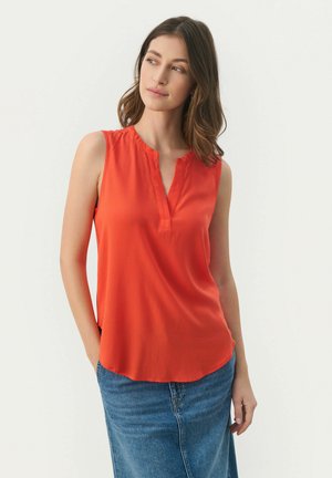 Blouse sans manches rouge avec un décolleté en V, fabriquée en tissu lisse. Présente une coupe décontractée et un ourlet arrondi, associée à une jupe en denim.