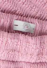 Tissu texturé rose avec un design à volants. Bretelle élastique blanche sécurisée avec un bouton transparent en détail.