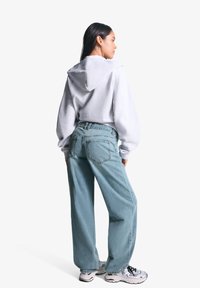 Hanorac gri cu glugă, cu croială largă, asociat cu blugi largi de culoare albastru deschis. Adidași argintii completează ținuta. Design simplu, fără modele.