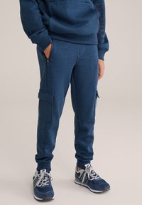 Mörkblå joggers i strukturerad tyg med cargo-fickor och en tapered design. Kombineras med blå och grå träningsskor.