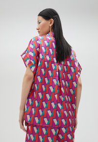 Colorful short-sleeve top featuring a geometric pattern in pink, red, and teal, with a loose fit and sleek, smooth texture.