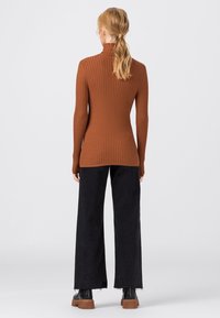 Brauner gerippter Rollkragenpullover kombiniert mit schwarzen weiten Hosen und klobigen schwarzen Stiefeln. Glatte Textur und enganliegende Silhouette.