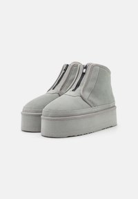 Bottines en suède gris avec une semelle plateforme, arborant des fermetures éclair latérales et des coutures contrastantes le long des bords.
