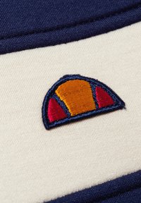 Parche bordado con un diseño semicircular en tonos naranja, rojo y azul sobre un fondo de tela color crema con ribete en azul marino.