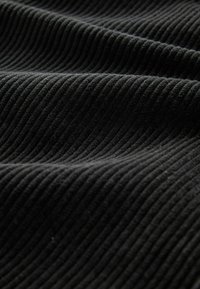 Schwarzer gerippter Stoff mit weicher Textur, der parallele Rillen in einem einheitlichen Muster aufweist und eine taktile Oberfläche schafft.