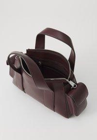 Borsa in pelle bordeaux con chiusura a zip, doppio manico superiore e tasca laterale. Texture liscia con dettagli di cucitura a contrasto.