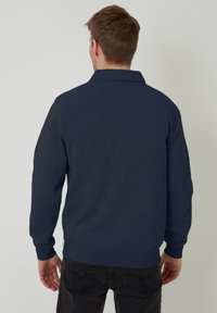 Navyblaues Sweatshirt mit Kragen und langen Ärmeln, das eine strukturierte Oberfläche aufweist. Der Saum und die Bündchen sind gerippt für eine bessere Passform.