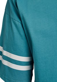 Grønblå bomulds-T-shirt med korte ærmer, der har tre hvide horisontale striber på ærmet. Glat tekstur og afslappet pasform.