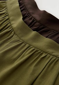 Deux jupes en tissu froncées, une vert olive et une brun foncé, montrant un gros plan des ceintures et de la texture plissée.