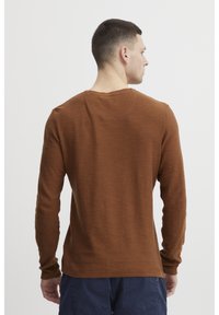 Brown long-sleeve shirt made of textured fabric, featuring a crew neck and a straight hem, viewed from the back, casual fit.