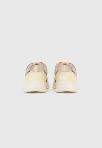 Μπεζ και κρεμ αθλητικά παπούτσια, σε προβολή από πίσω, σε ουδέτερο φόντο, που παρουσιάζουν μαλακές φτέρνες και υφασμάτινες λεπτομέρειες με υφή.