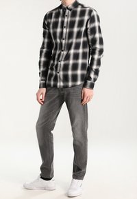 Zwart-wit geruite blouse met lange mouwen en een knoopsluiting, gecombineerd met een grijze spijkerbroek en witte sneakers, wat zorgt voor een casual look.