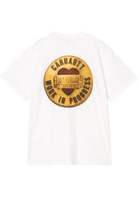 Camiseta de algodón blanca con un gran gráfico redondo en la parte posterior que presenta texto en marrón y rojo que dice "CARHARTT WORK IN PROGRESS" y un diseño de camión.