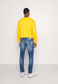Gul sweatshirt, blå jeans och vita sneakers. Slät textur, passande design, standard bakvy, minimal märkning på jeansen.