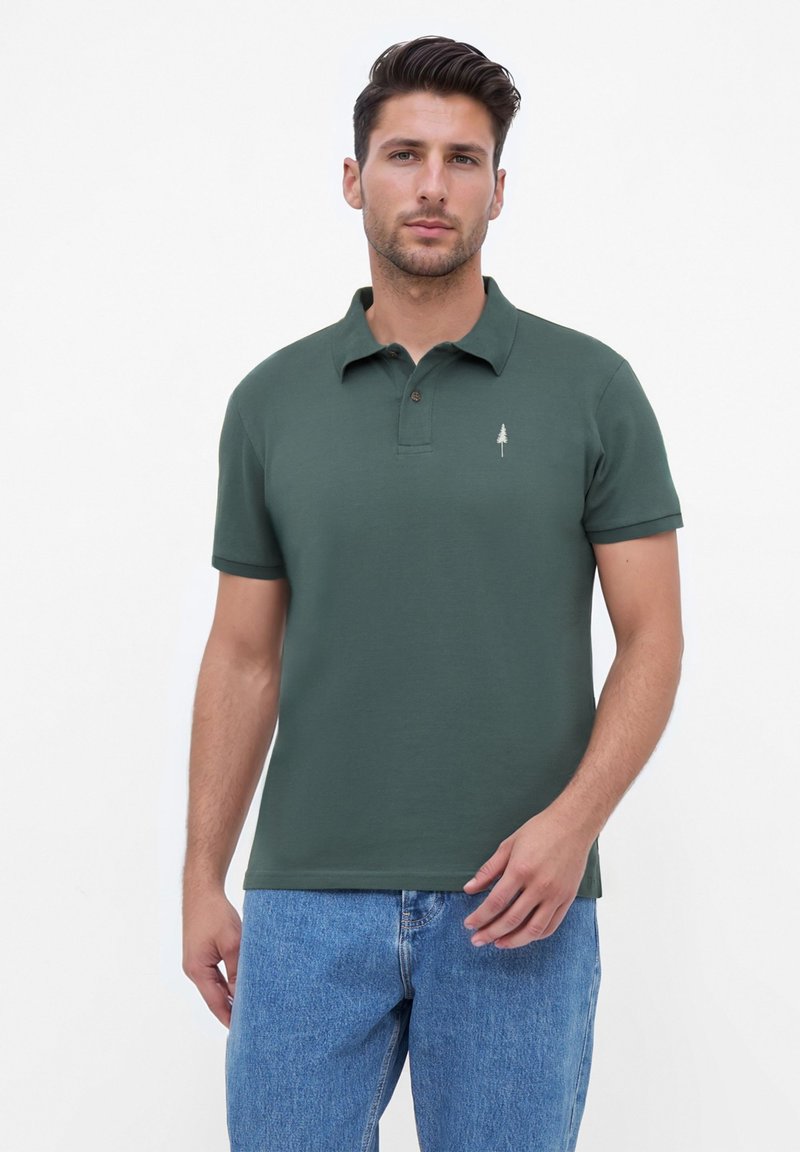 Polohemd aus dunkelgrünem Baumwollstoff mit einem klassischen Kragen, zwei Knöpfen und einem dezenten Baum-Logo, das auf der linken Brust gestickt ist.