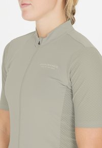 Lähikuva henkilöstä, joka käyttää vaaleanharmaata, lyhythihaista pyöräilypaitaa, jossa on teksturoidut hihat ja rintaan painettu teksti "Endurance Hero of the Road".