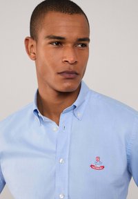Lichtblauw button-up overhemd van katoen met een zachte textuur. Heeft een klein rood geborduurd logo op de linkerborst.