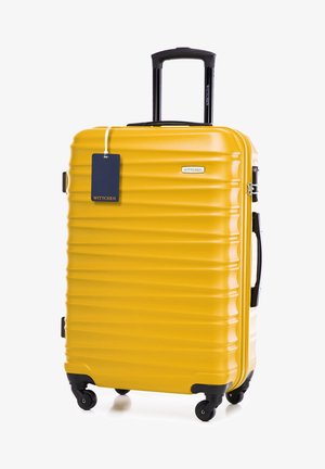 Žlutý kufr s vroubkovaným tvrdým pláštěm, černou rukojetí a koly, kovovým zipem a připojenou visačkou. Logo viditelné na boku.