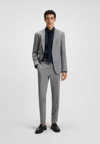 Grå, slim-fit kostym med ett subtilt rutmönster, tillsammans med en mörk skjorta och svarta loafers. Skräddarsydd design med strömlinjeformad siluett.