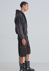 Hanorac negru cu un finisaj texturat, asortat cu pantaloni scurți cargo până la genunchi, cu buzunare laterale. Accesoriile includ cizme negre cu buclă.