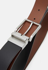 Cintura in pelle marrone e nera con fibbia rettangolare in metallo argentato con marchio inciso e finitura testurizzata.